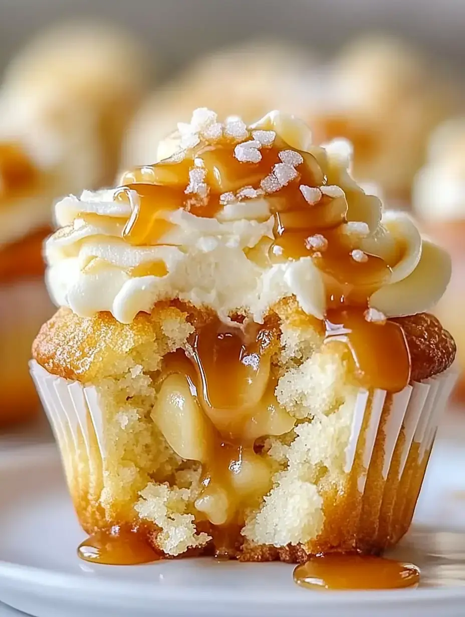 A close-up of a cupcake with a creamy frosting topped with caramel drizzle and sugar crystals, revealing a gooey filling inside.