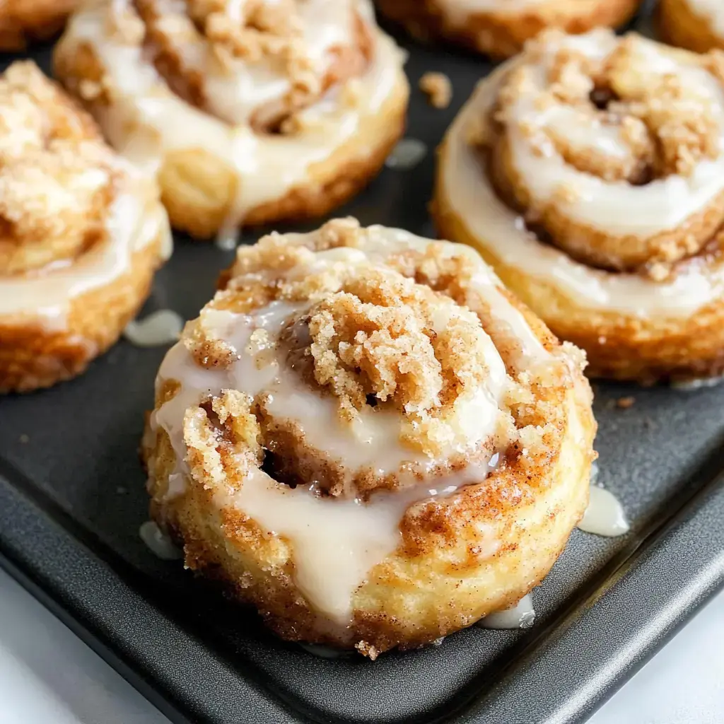 Golden cinnamon rolls glazed with icing and streusel, fresh out of the oven on a black sheet.