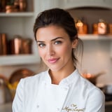 A woman in a white chef's coat smiles for the camera.