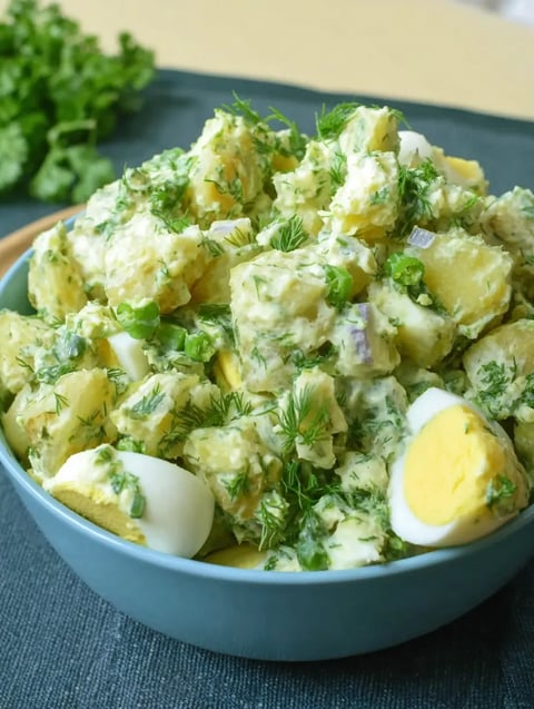 A blue plate packed with chunks of potato, slices of egg, and onion bits.
